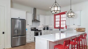 A modern kitchen with white cabinetry, a stainless steel refrigerator, a central island with red bar stools, and pendant lighting. - The Lamar Landing (Oxford)