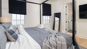 A modern bedroom with a four-poster bed, blackout curtains, a flat-screen TV, and a large mirror. - The Lamar Landing (Oxford)