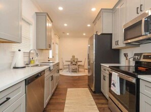 A modern kitchen with stainless steel appliances, white cabinetry, and a dining area with a table and chairs. - Meadow Crest (Oxford)