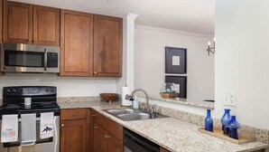 A kitchen with wooden cabinets, stainless steel appliances, granite countertops, and blue vases. - Spacious Condo Close to Ole Miss and Hospital (Oxford)
