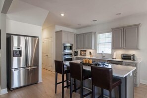 A modern kitchen with a stainless steel refrigerator, a built-in oven, a gas stove, and a small island with bar stools.
