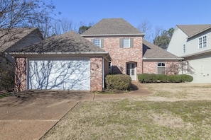 A two-story house with a garage, a brick exterior, and a well-maintained lawn.