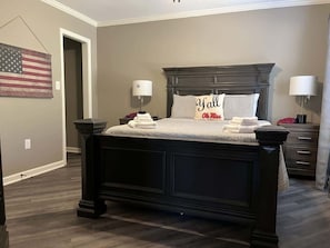 A bedroom with a dark wooden bed, a checkered bedspread, two bedside lamps, and an American flag on the wall. - Great Location 3 Bedroom 3 Bathroom Condo (Oxford)