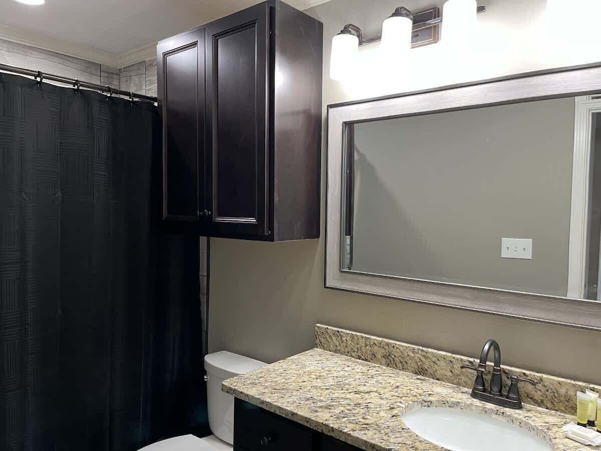A bathroom with a dark shower curtain, a sink with a granite countertop, and a large mirror above the sink.