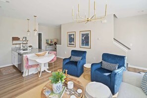 A modern living room with a dining area, blue velvet armchairs, a chandelier, and artwork on the walls. - The Blue Nest (Oxford)