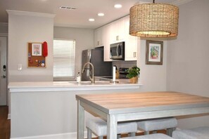 Una cocina moderna con armarios blancos, electrodomésticos de acero inoxidable, una mesa de comedor de madera y una lámpara colgante de fibras naturales.