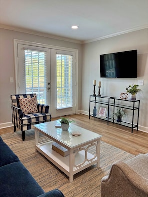 A living room with a sofa, a coffee table, a TV mounted on the wall, and a door with blinds. - The Rebel House (Oxford)