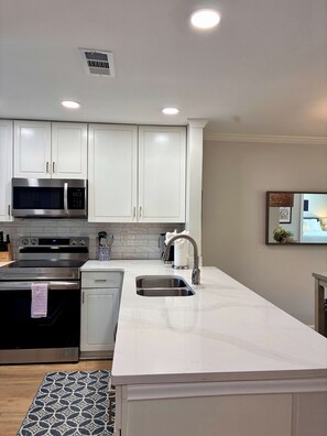 A modern kitchen with white cabinetry, stainless steel appliances, and a marble countertop. - The Rebel House (Oxford)