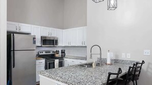 Una cucina moderna con mobili bianchi, elettrodomestici in acciaio inossidabile, un piano di lavoro in granito e un angolo bar con sgabelli.