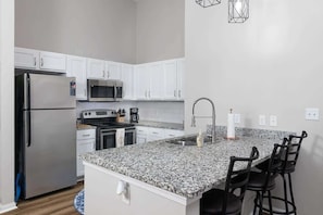 Una cocina moderna con armarios blancos, electrodomésticos de acero inoxidable, una encimera de granito y una zona de bar con taburetes.