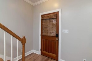 Una porta in legno con una finestra, battiscopa bianco e un interruttore sulla parete.