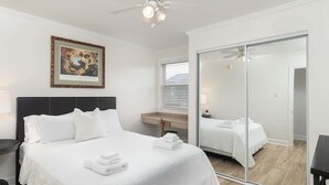 Een hotelkamer met een bed, een plafondventilator, een inlijsting afbeelding aan de muur, een spiegel en een schuifdeur.
