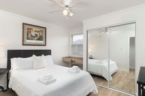 Hotellihuone, jossa on sänky, kattotuuletin, seinällä oleva taulu, peili ja liukuovi.