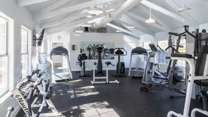 Een sportschool met diverse fitnessapparaten, een waterpunt en een plafond met zichtbare balken.