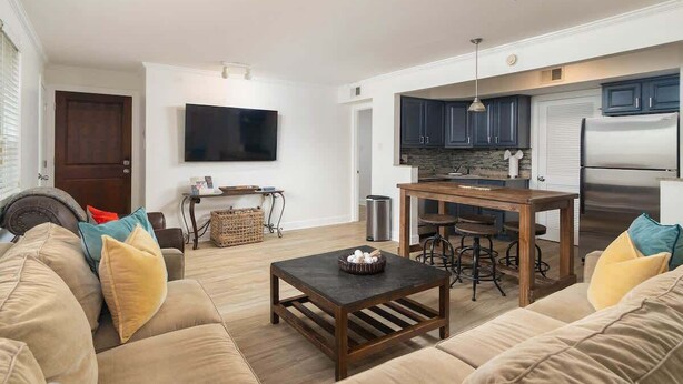 Een moderne woonkamer met een bank, salontafel en televisie. Er is een keuken met een koelkast, fornuis en eettafel.