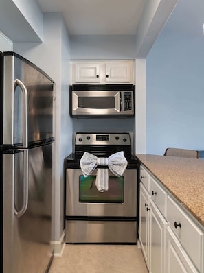 A kitchen with a stainless steel refrigerator, a microwave, and an oven. There is a striped cloth hanging over the oven door. - Gated Condo, Close to Ole Miss! (Oxford)