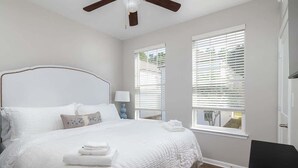 Ein Schlafzimmer mit einem großen Bett, einem Deckenventilator und zwei Fenstern mit Jalousien.