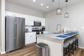 Una cocina moderna con electrodomésticos de acero inoxidable, armarios blancos, encimera de granito y una zona de taburetes de bar.
