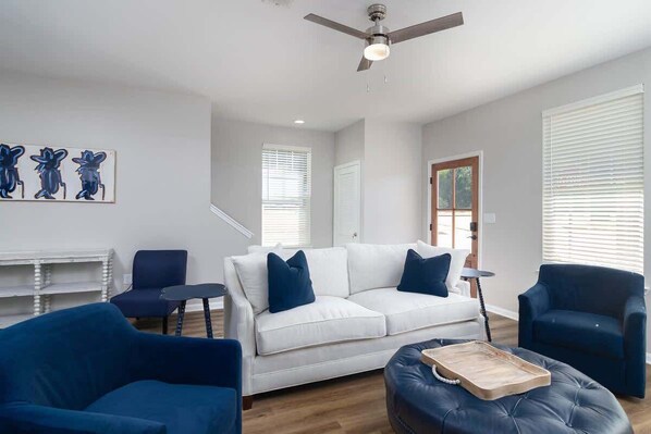 Una sala de estar moderna con un sofá blanco, sillones azules, una mesa de centro de madera y un ventilador de techo.