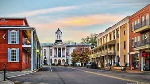 A street view with a prominent building with a clock tower, a red brick building with a sign, and a yellow building with a balcony. - Welcome to the 50 YARD LINE! (Oxford)