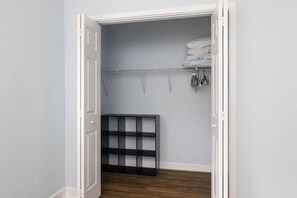 Ein begehbarer Kleiderschrank mit einem Metallregal, einem ausgeklappten Bett und hängender Kleidung.