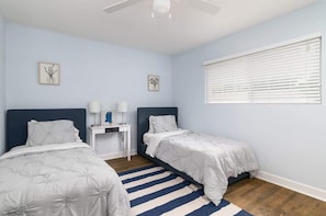 Une chambre avec deux lits, un bureau et une fenêtre avec des stores.