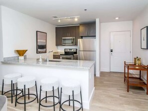 A modern kitchen with a central island, bar stools, stainless steel appliances, and a wooden dining table. - The Middle Ground (Oxford)