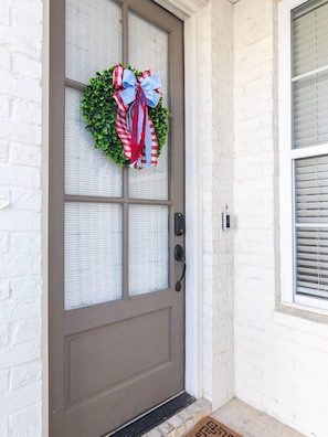 A door with a frosted glass panel, a wreath with a red and white ribbon, and a doormat.