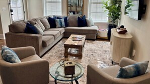 A living room with a sectional sofa, two armchairs, a coffee table, a glass side table, a mirror, and a potted plant. - Rebel Retreat at The Mill (Oxford)