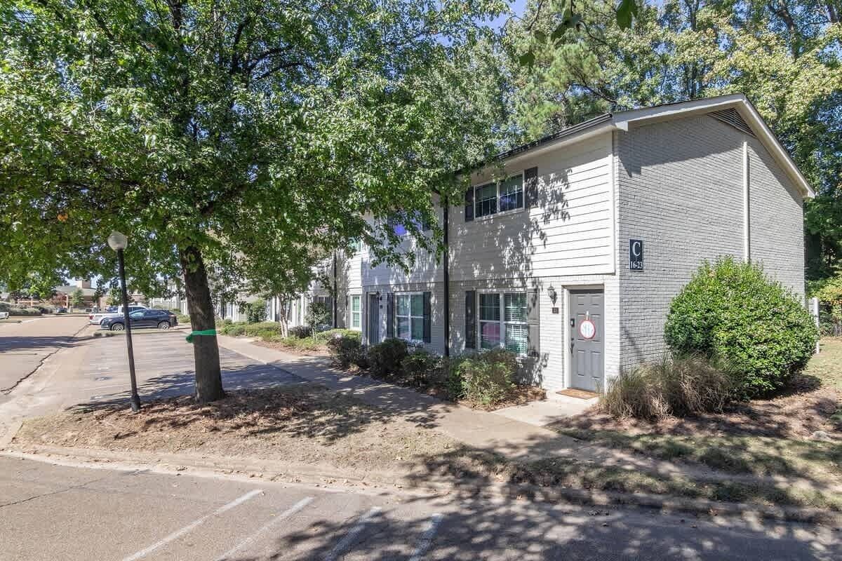 A two-story building with a garage door, a mailbox, and a small bush in front.
