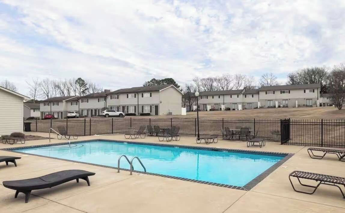 A swimming pool with lounge chairs and a fenced area, surrounded by apartment buildings.