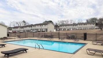 A swimming pool with lounge chairs and a fenced area, surrounded by apartment buildings.