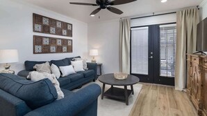Ein Wohnzimmer mit einer Couch, einem Couchtisch, einem Deckenventilator und einer Tür mit Jalousien.