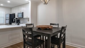 Eine moderne Küche mit weißen Schränken, einem schwarzen Kühlschrank und einem Holzes Esstisch mit vier Stühlen.