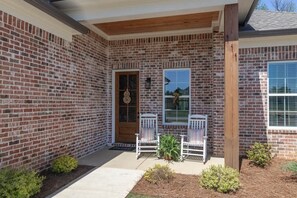 A brick house with a front porch, two white chairs, and a small garden. - Retreat in Blue (Oxford)