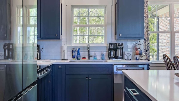 Een moderne keuken met donkerblauwe kastjes, roestvrijstalen apparatuur en een houten vloer.