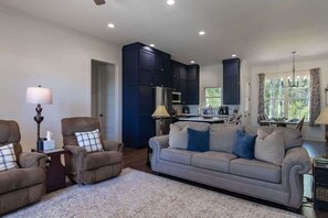 A living room with a sofa, armchairs, a coffee table, and a rug. There is a kitchen area with cabinets and appliances. - Retreat in Blue (Oxford)