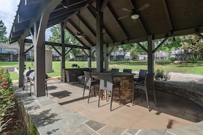 An outdoor patio with a stone bar and seating, surrounded by a covered area with a ceiling fan. - The Haven at Old Taylor Place (Oxford)