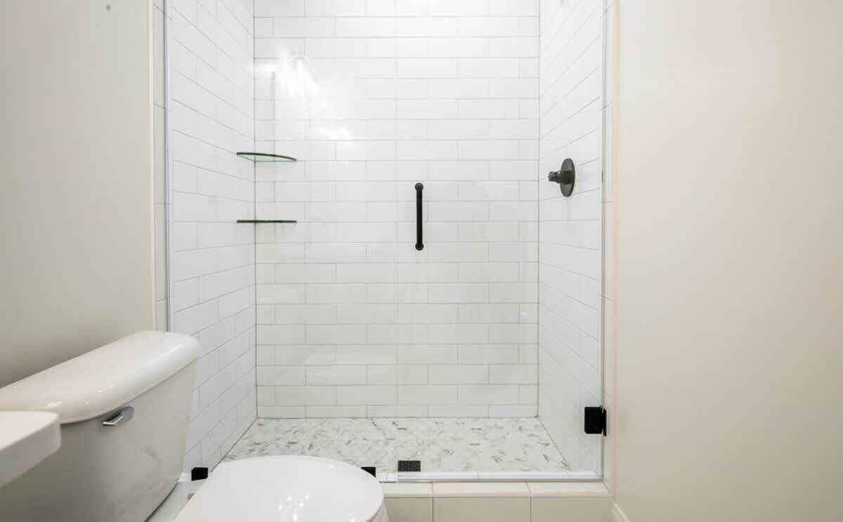 Ein kleines Badezimmer mit weißen Wänden, einer Toilette, einer Duschkabine aus Glas und einem Marmorboden.