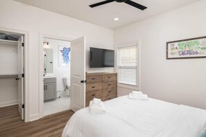 Een slaapkamer met een bed, een dressoir, een televisie en een deur naar een badkamer.
