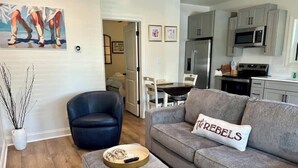 Ein modernes Wohnzimmer mit einem grauen Sofa, einem schwarzen Sessel und einem Essbereich mit einem weißen Tisch und Stühlen.
