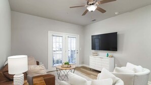 A modern living room with a ceiling fan, a flat-screen TV, a sofa, a coffee table, and a window with blinds. - The Modern Sip (Oxford)