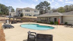 A swimming pool with lounge chairs, a covered patio area, and a building with a garage. - The Modern Sip (Oxford)