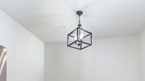 A dining area with a round table, four chairs, a hanging light fixture, and a refrigerator. - The Modern Sip (Oxford)