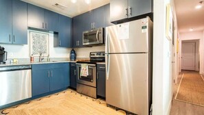 A modern kitchen with blue cabinets, stainless steel appliances, and a wooden floor.