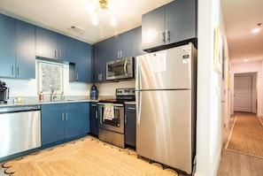 A modern kitchen with blue cabinets, stainless steel appliances, and a wooden floor.