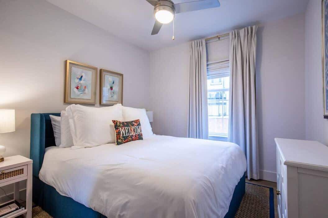 A hotel room with a bed, a nightstand, a ceiling fan, and a window with curtains.