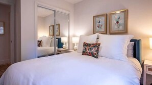 A hotel room with a large bed, a wardrobe, two bedside lamps, and two framed artworks on the wall.