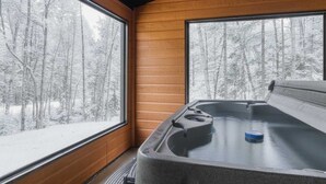 Uma banheira de hidromassagem com vista para uma floresta coberta de neve através de grandes janelas.