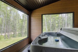 Un jacuzzi con vistas a un bosque a través de amplias ventanas.
